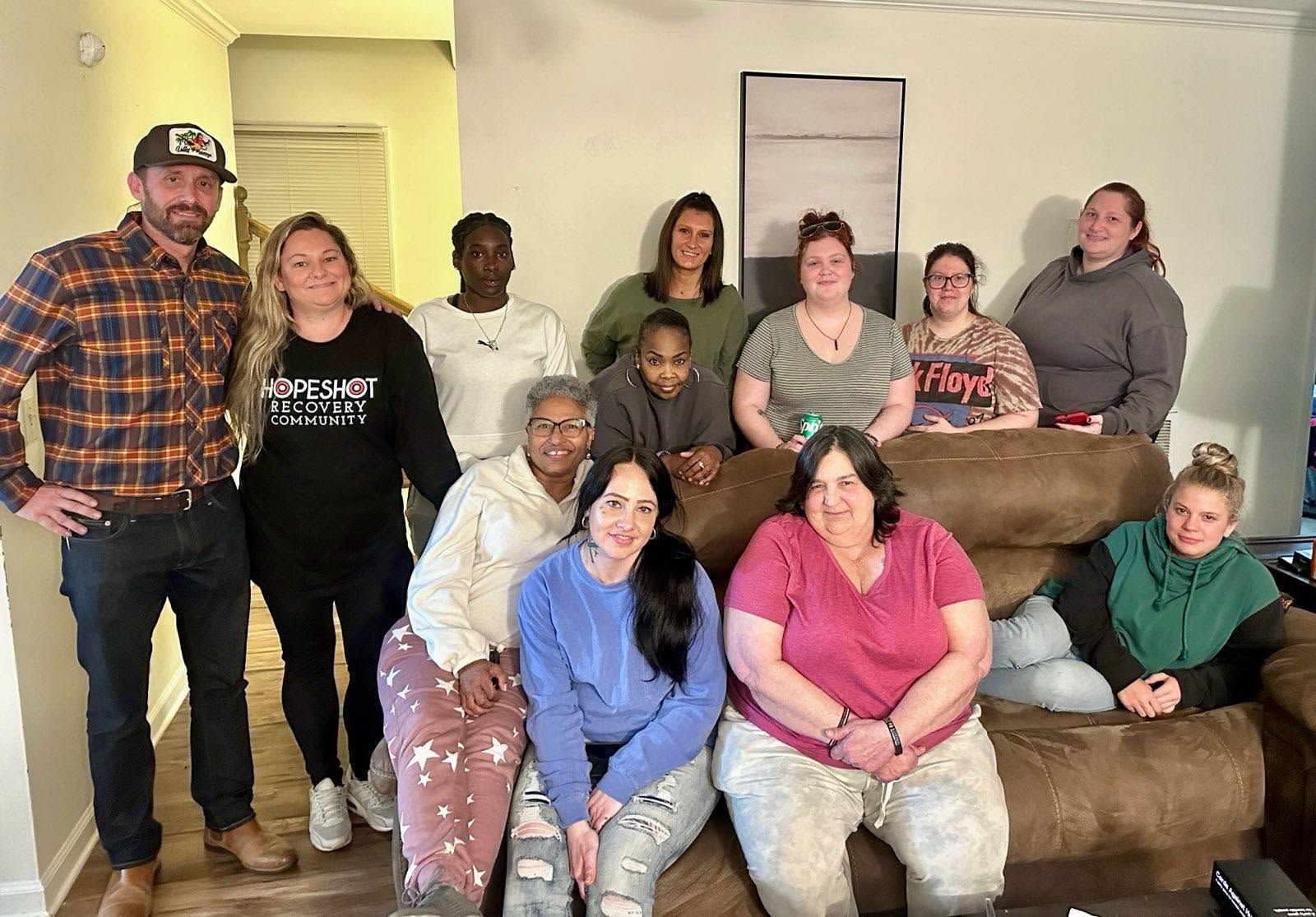 Group of people posing together in a living room beside a brown couch