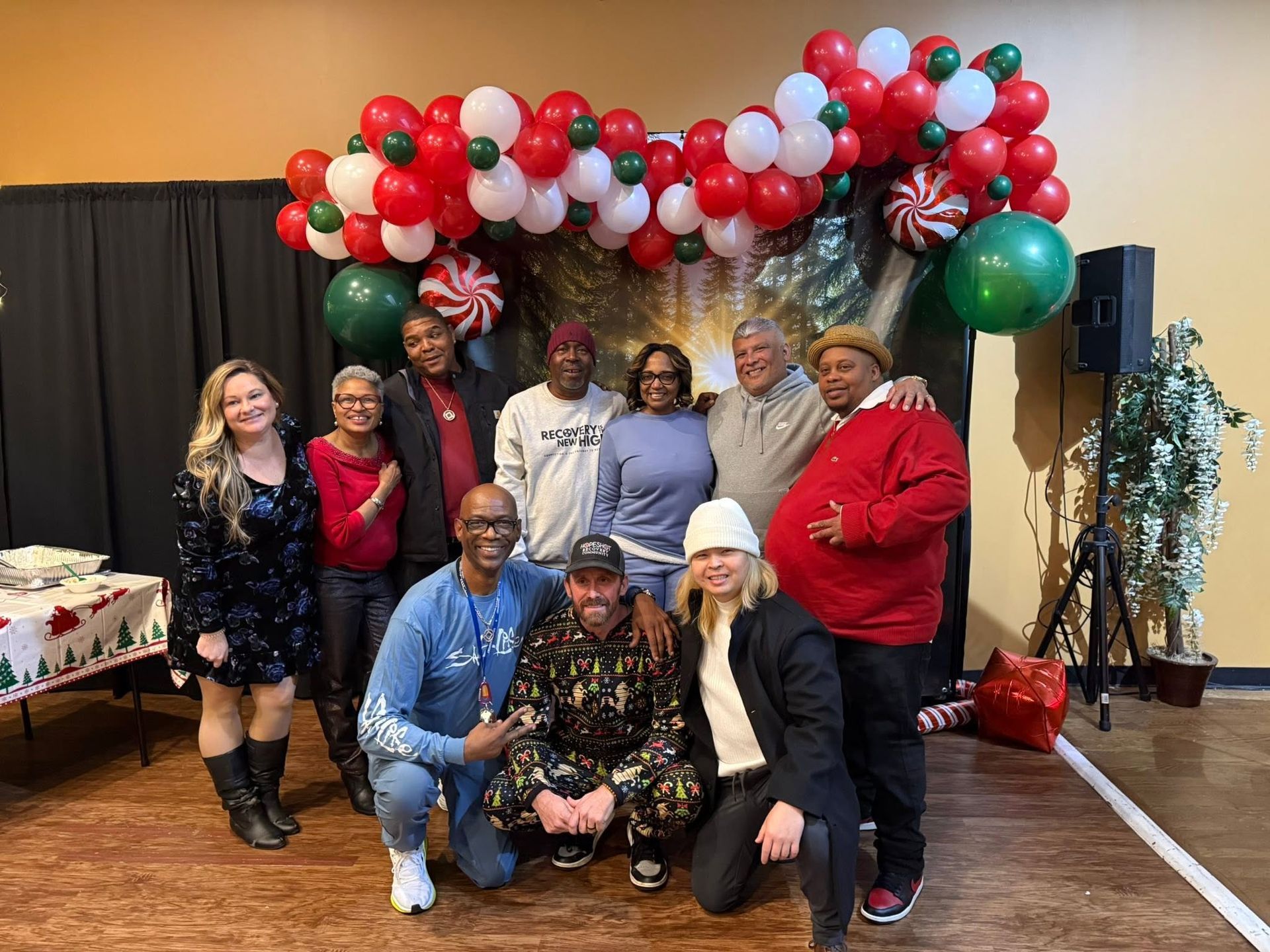 Group posing indoors under red, white, and green balloon arch at a festive event