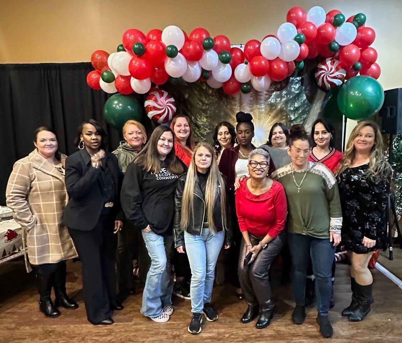 Group posing indoors under a red, white, and green balloon arch, smiling at a celebration event