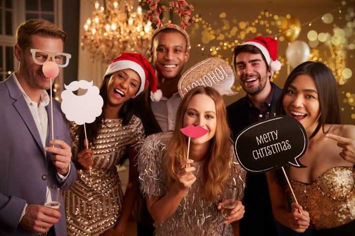 Friends in festive attire posing with holiday props at a Christmas party, smiling before a warm bokeh backdrop
