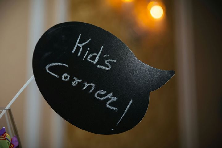 Black speech-bubble sign reading “kids corner” on a blurred indoor background