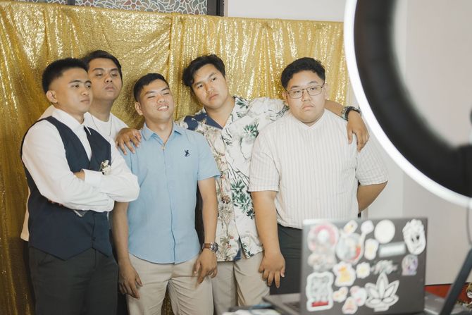 Five people posing in front of a gold backdrop, with a laptop covered in stickers in the foreground.