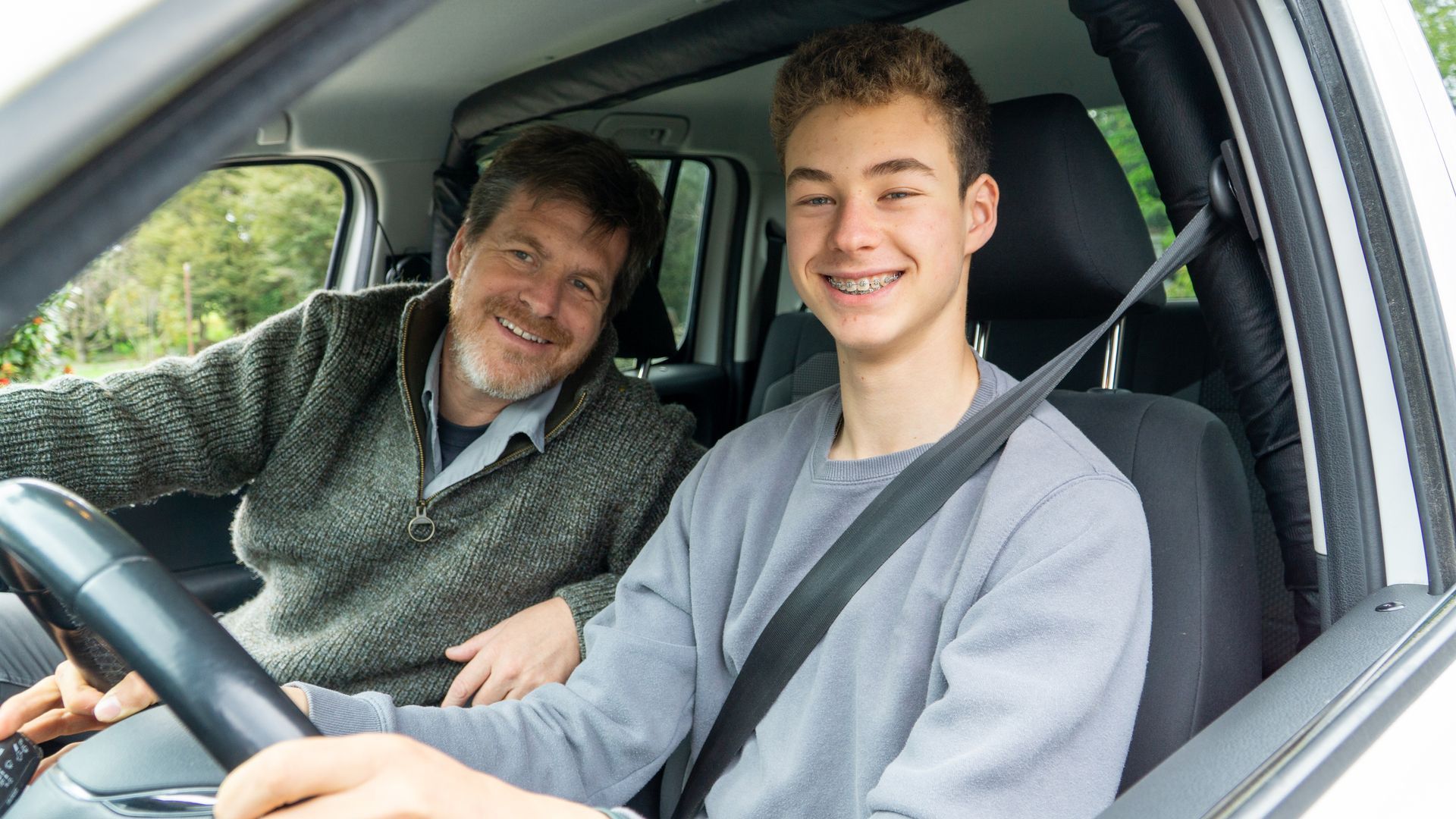 A man is teaching a young boy how to drive a car.