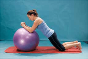 Uma mulher está ajoelhada em um tapete ao lado de uma bola de exercícios roxa