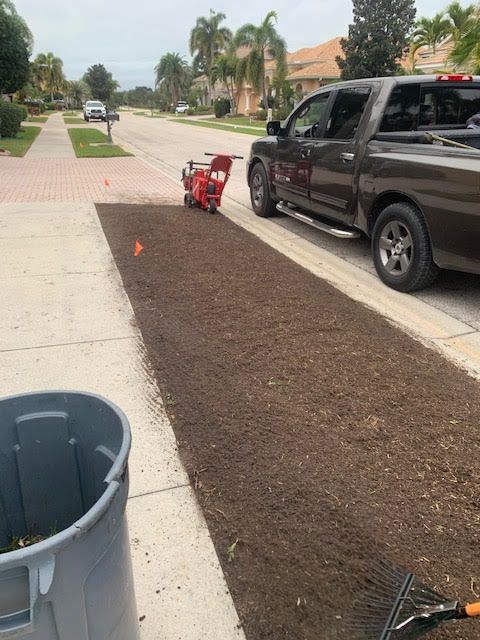 A dark pickup truck parked on a residential street next to a long rectangular patch of freshly leveled brown soil.