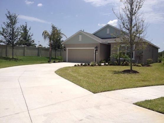 A single-story suburban house with a tan exterior, a two-car garage, and a concrete driveway under a blue sky.