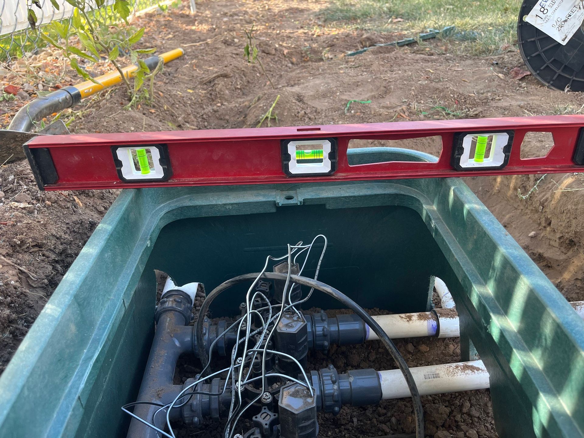 Open utility box with pipes, wires, and a red spirit level resting across the top outdoors