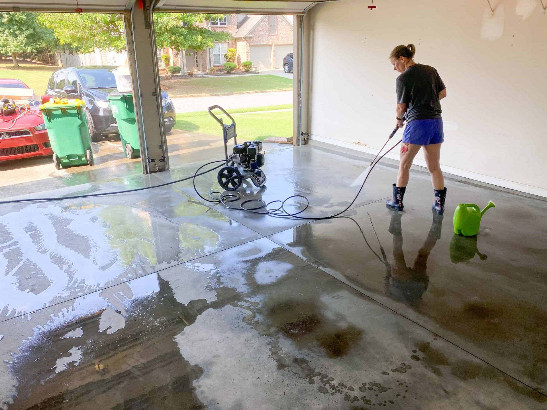 A woman is using a high pressure washer to clean a garage floor.