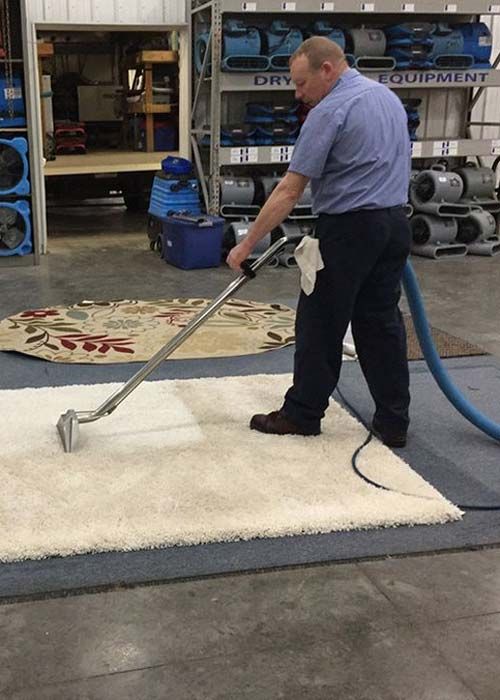 A man is cleaning a rug with a vacuum cleaner