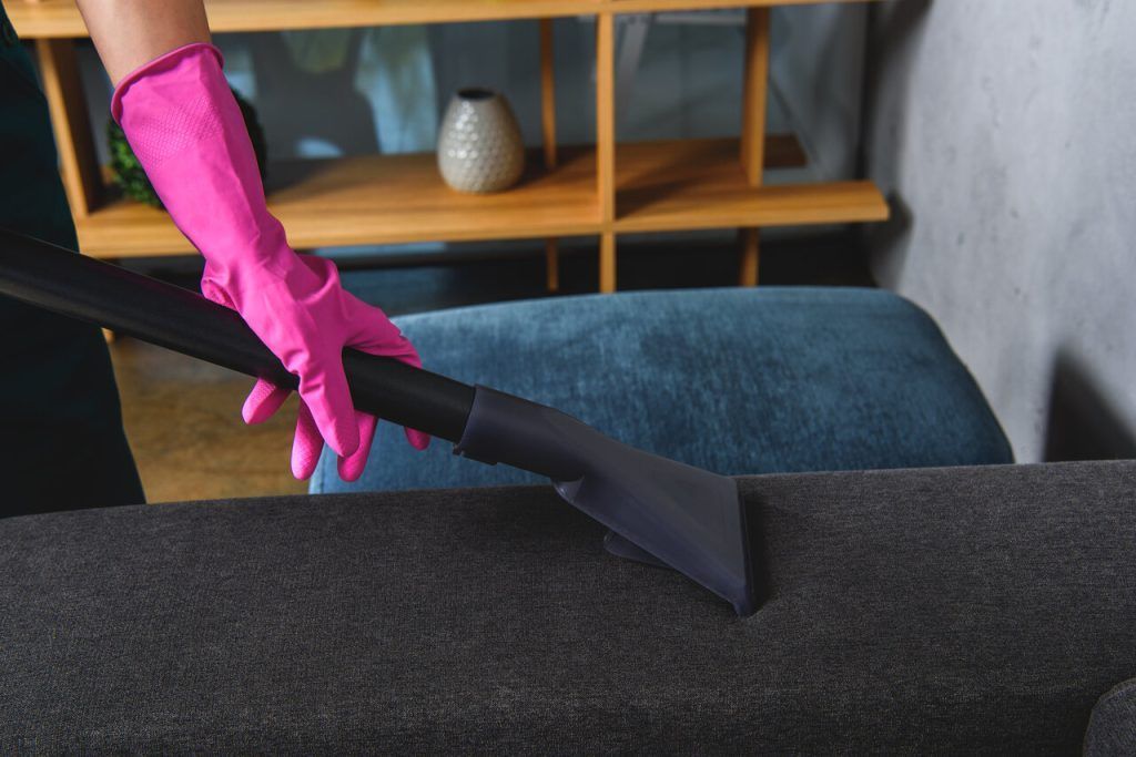 A woman in pink gloves is cleaning a couch with a vacuum cleaner.