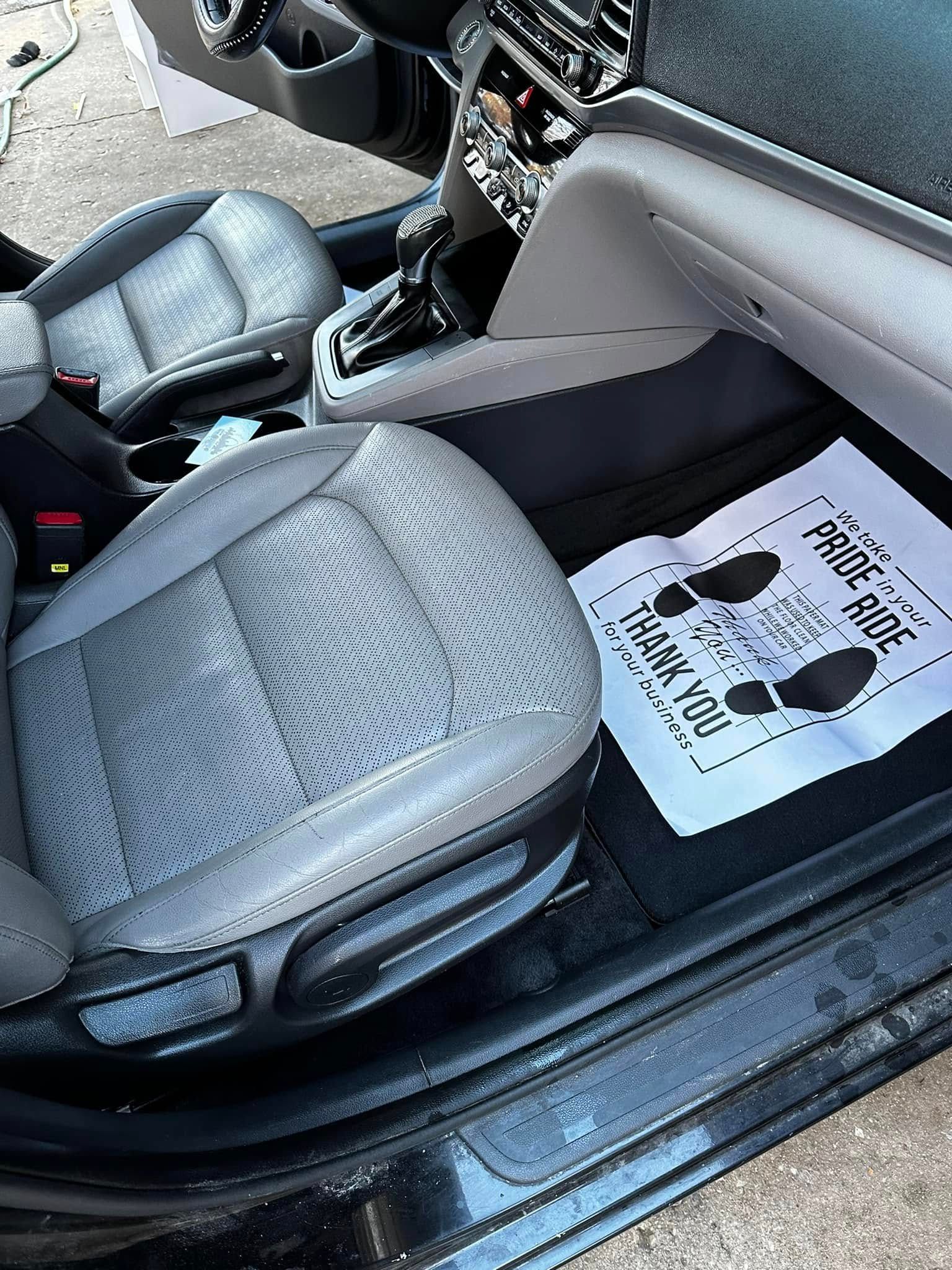 Interior of a car with gray leather seats and a white floor mat in the front passenger footwell
