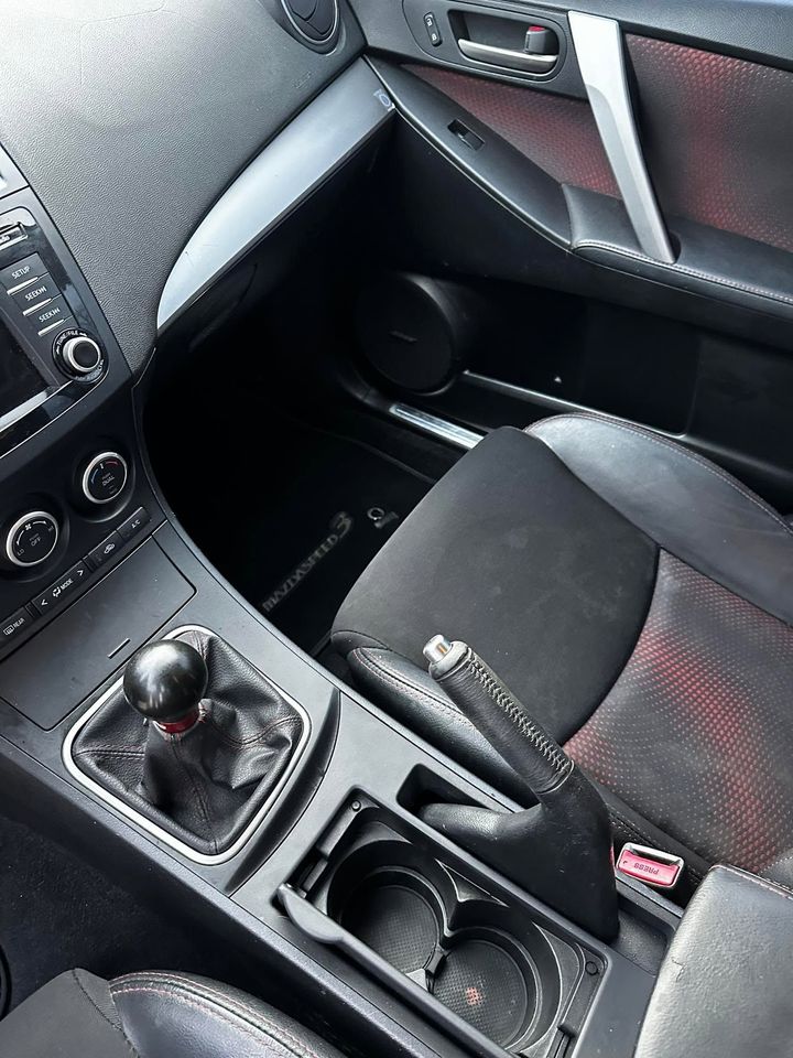 Car interior with manual gear shift, cup holders, and black seats with red stitching