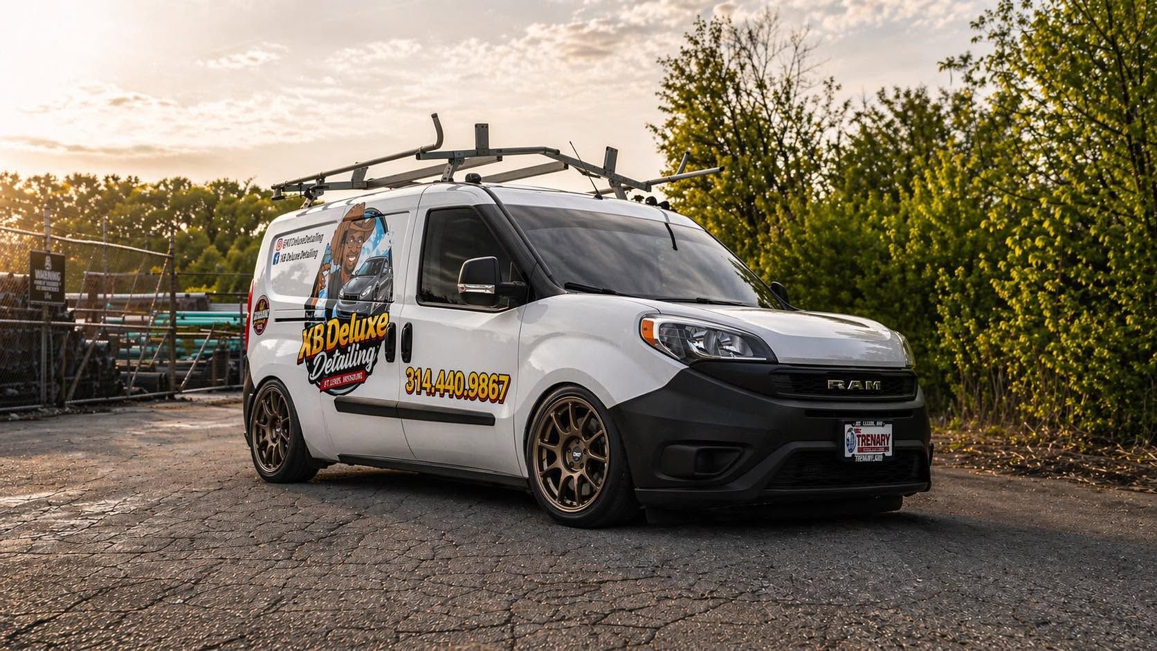 White cargo van with roof rack parked on gravel at sunset, side decals visible.