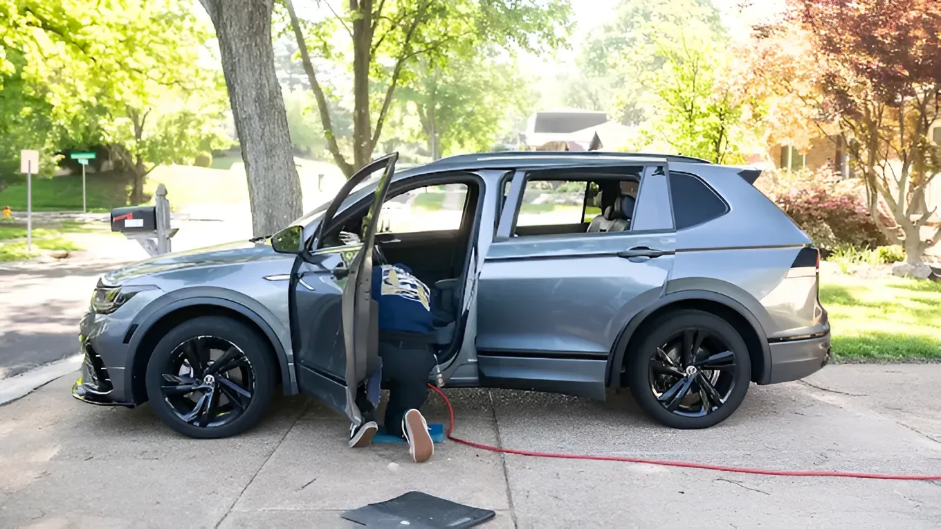 Gray SUV with open door; person crouches beside it on a sunny suburban street