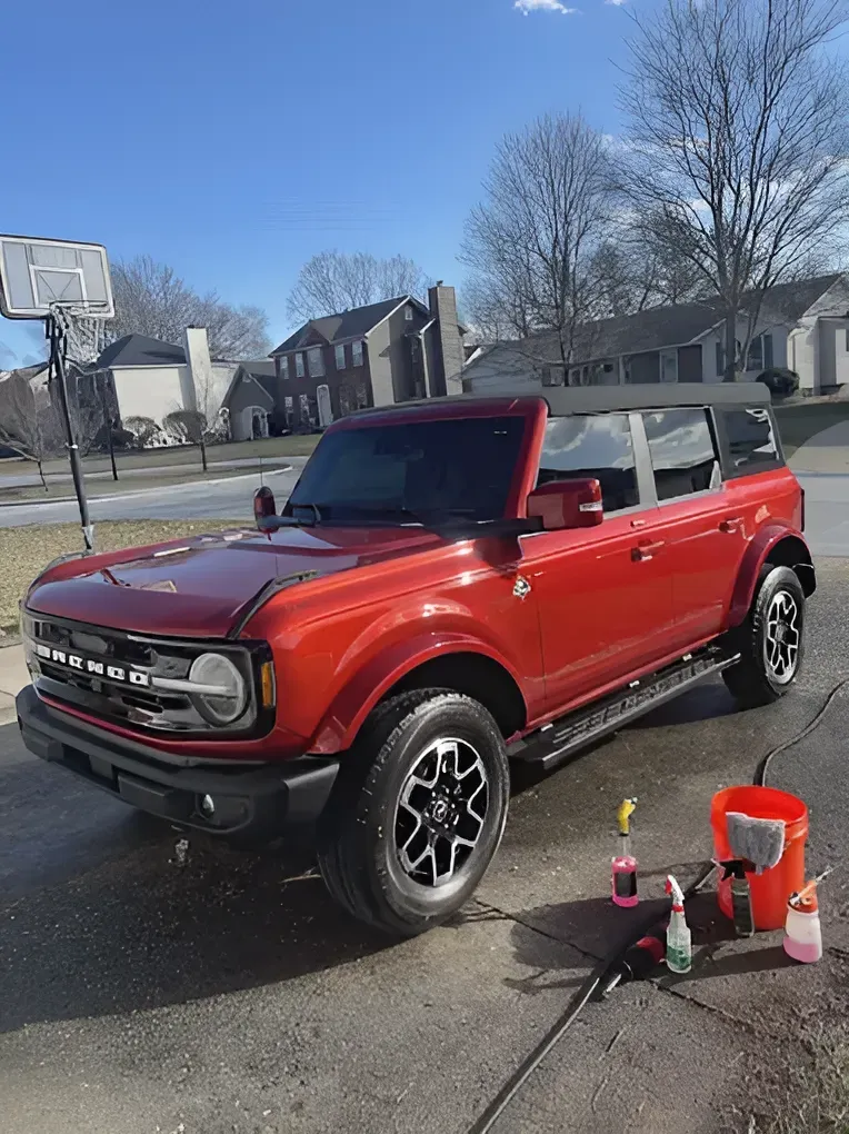 Red convertible SUV parked in a driveway, with car wash supplies beside it on a sunny suburban street.