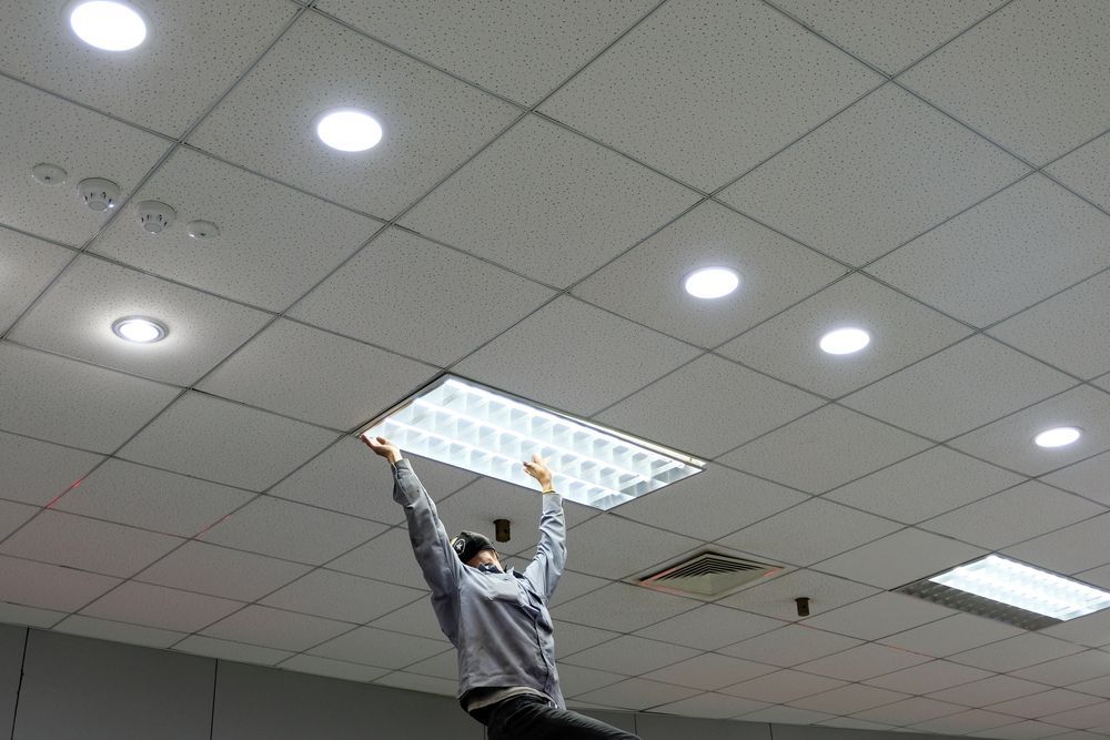 Person Holding a Rectangular Ceiling Light in a Grid Ceiling, Inside a Building — Do Right Electrical in Redlynch, QLD
