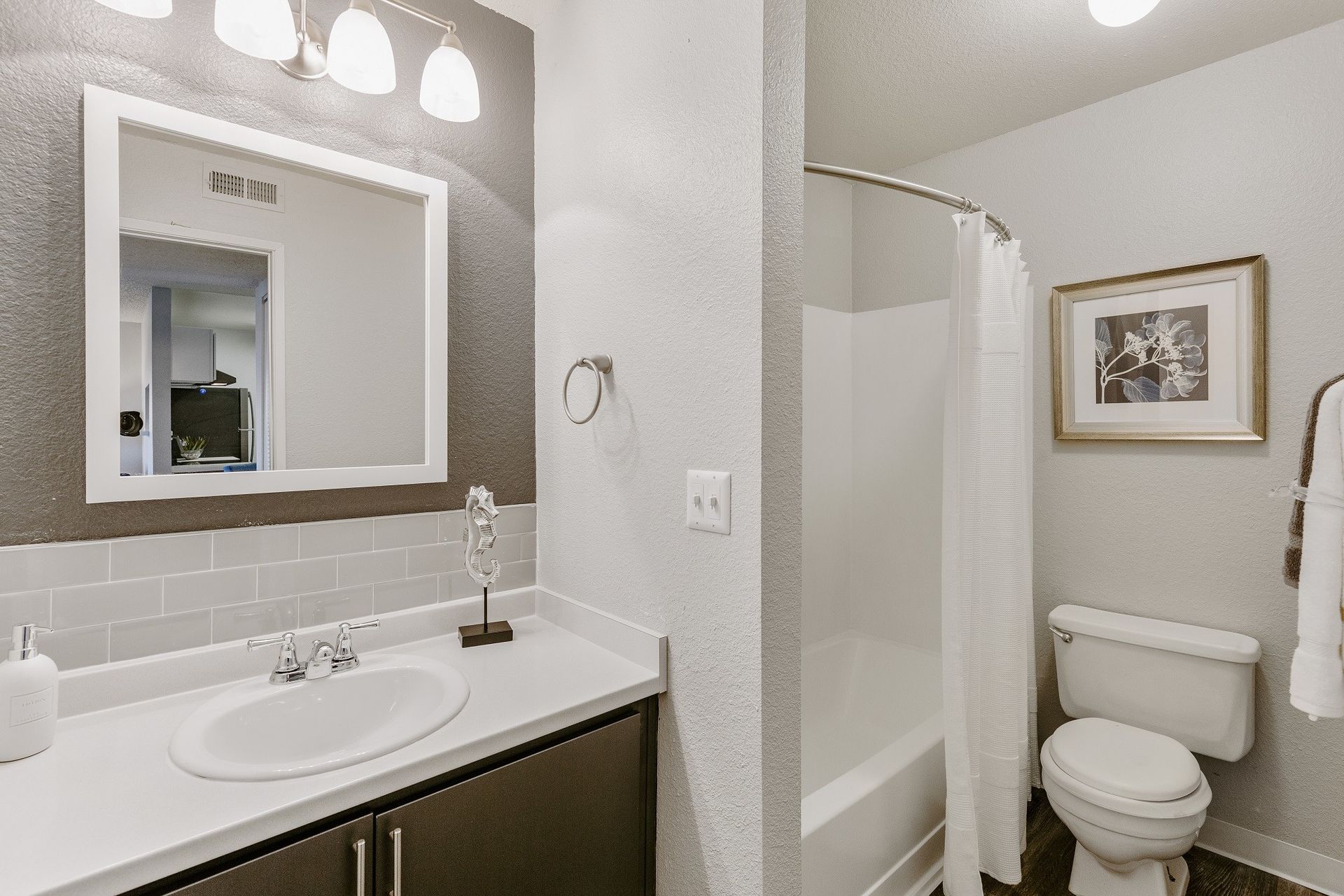 Bathroom with a sink, toilet, and shower/tub. White walls, grey accents, and a framed picture at Westward Heights in Denver, CO.