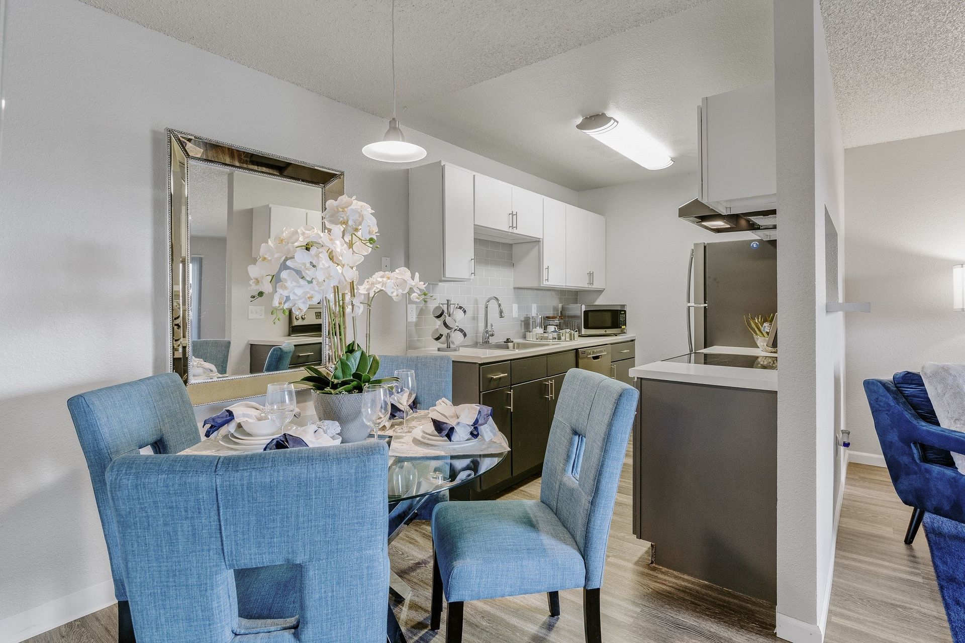 Dining area with blue chairs, mirrored wall, and kitchen in the background at Westward Heights in Denver, CO.