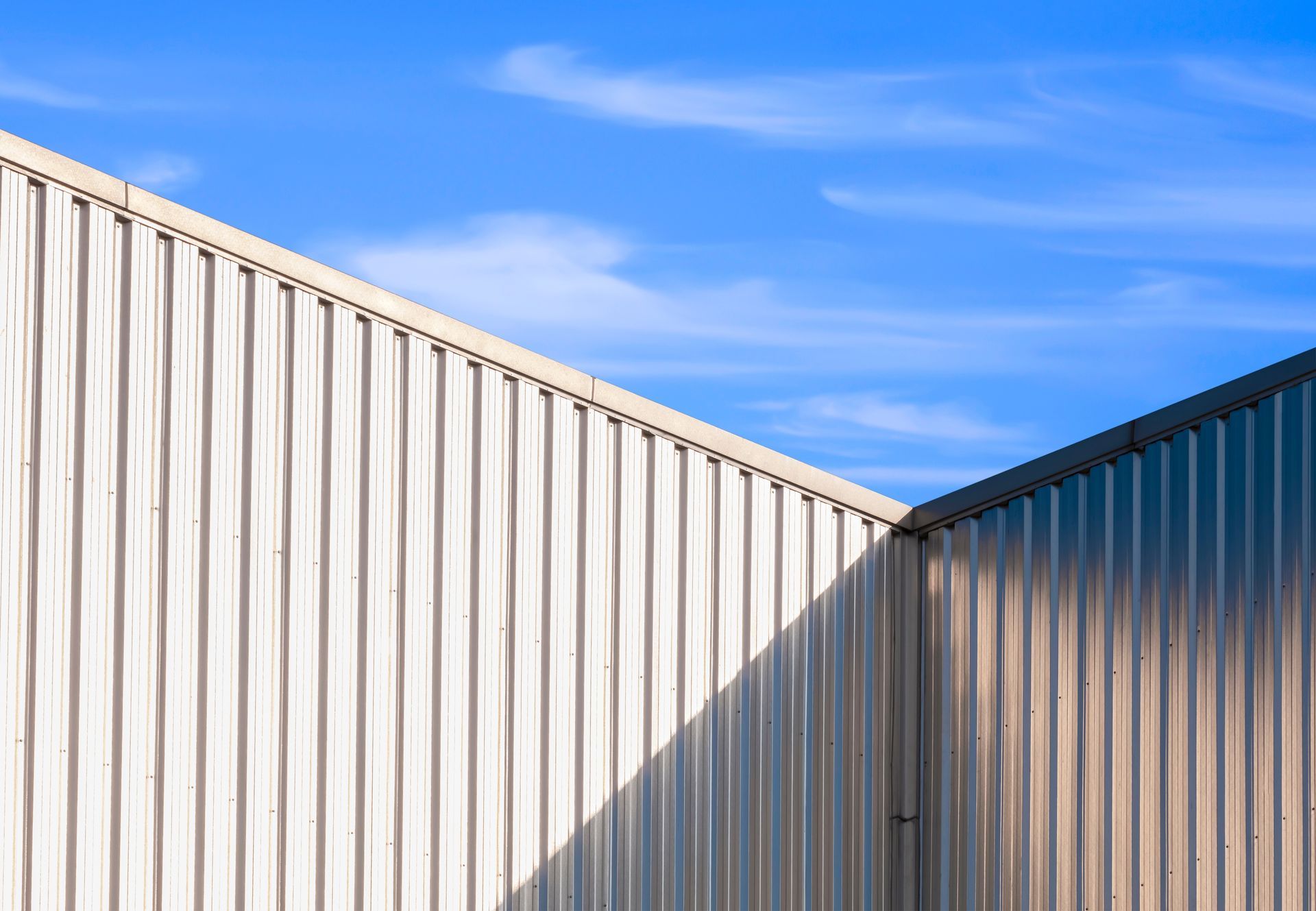 White corrugated metal building walls against a bright blue sky with wispy clouds.