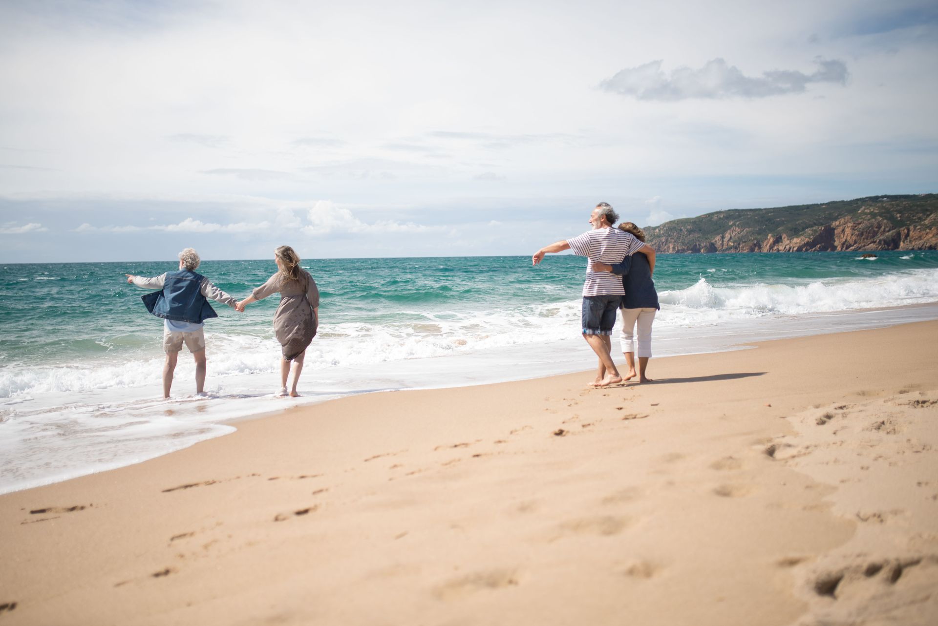 People standing on a sandy beach by turquoise waves under a bright, cloudy sky