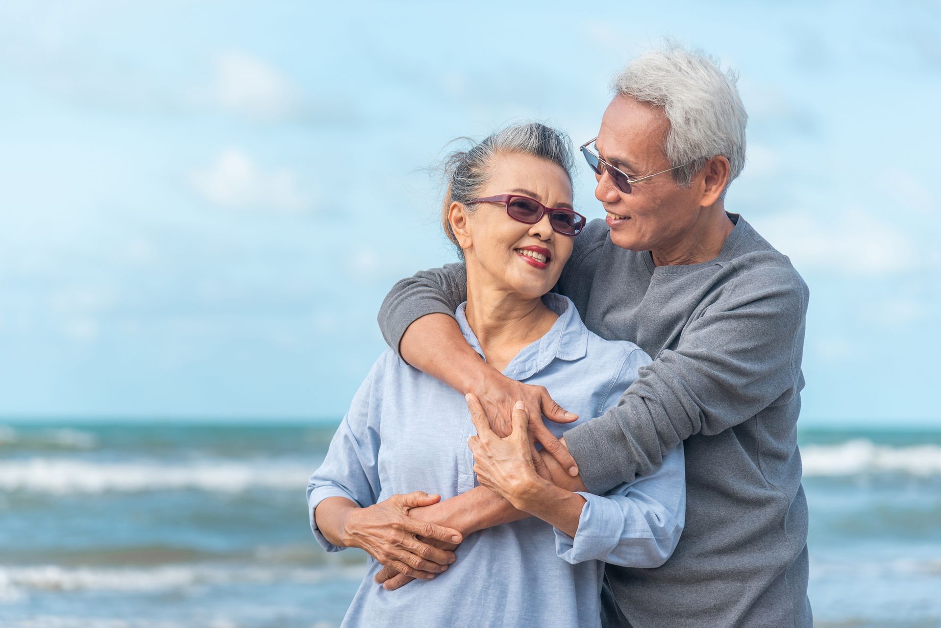 Smiling couple embracing on a beach, with the ocean and blue sky in the background