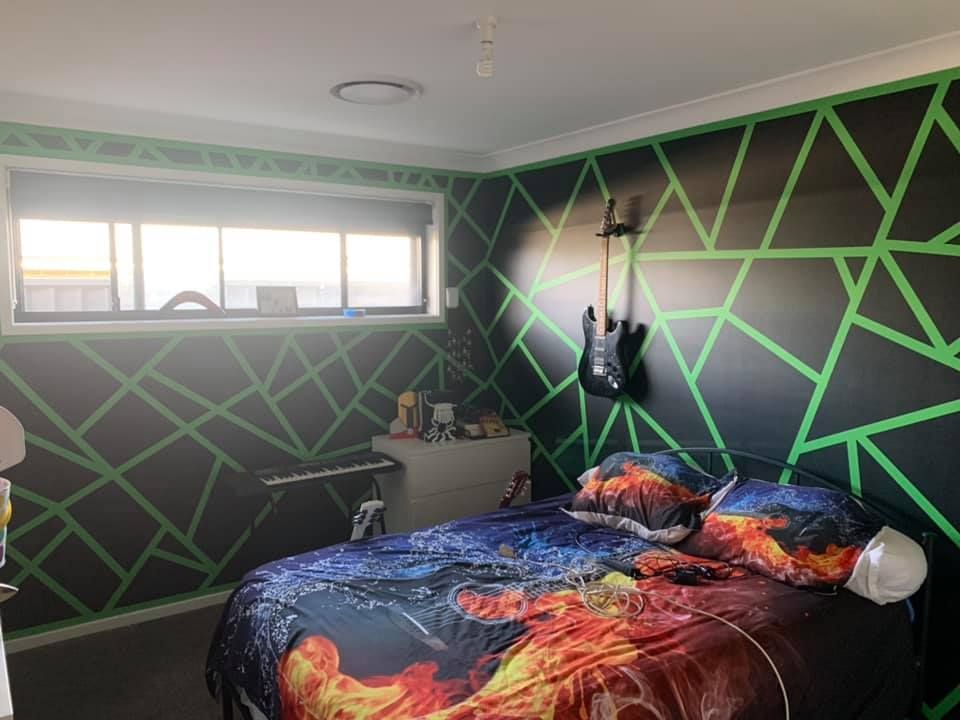 Bedroom with a black geometric accent wall with green tape, guitar, bed, and window.