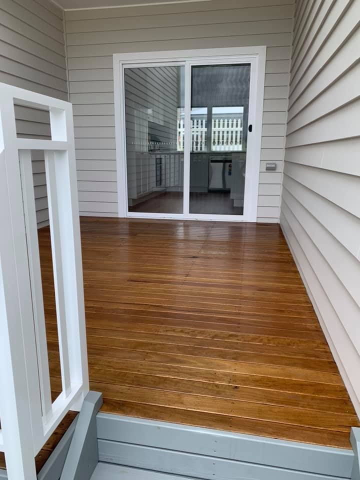 Wooden deck with sliding glass door, white railing, and grey steps.
