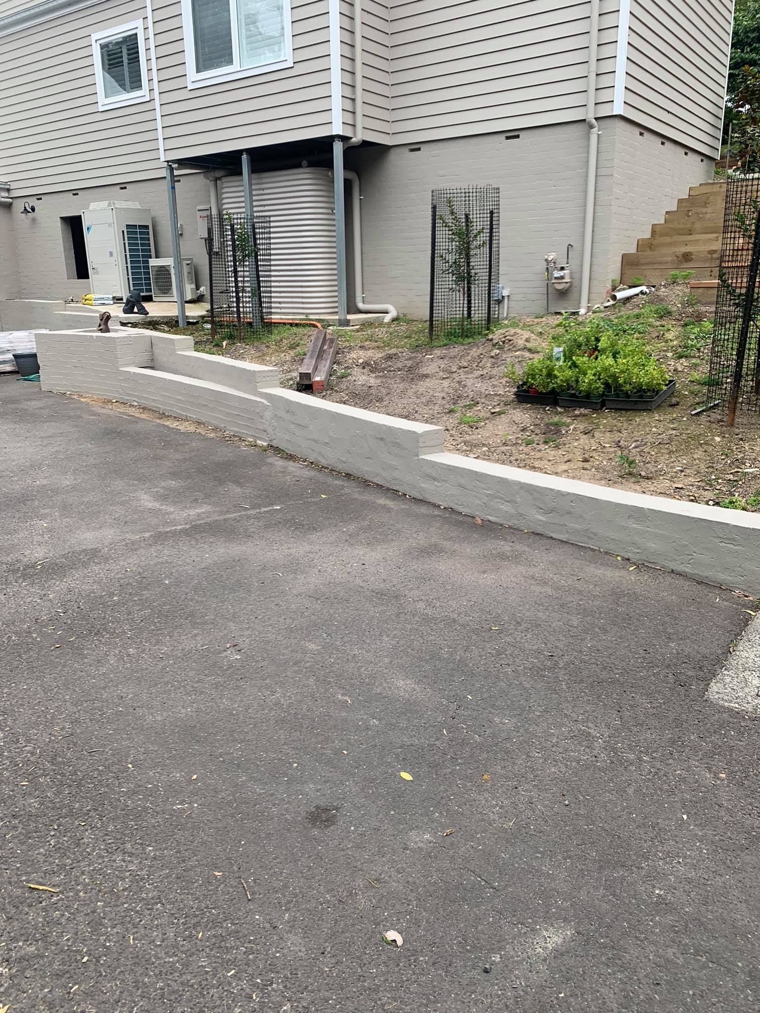 Asphalt driveway next to a concrete retaining wall with a building in the background.