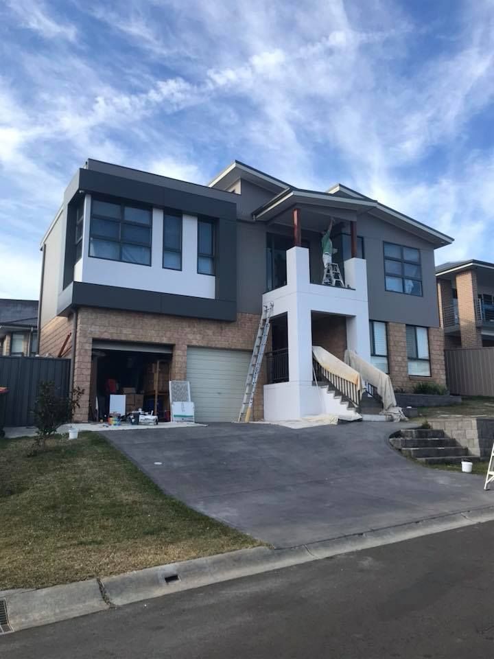 Two-story house with gray and white exterior being painted. A ladder is propped against the front.
