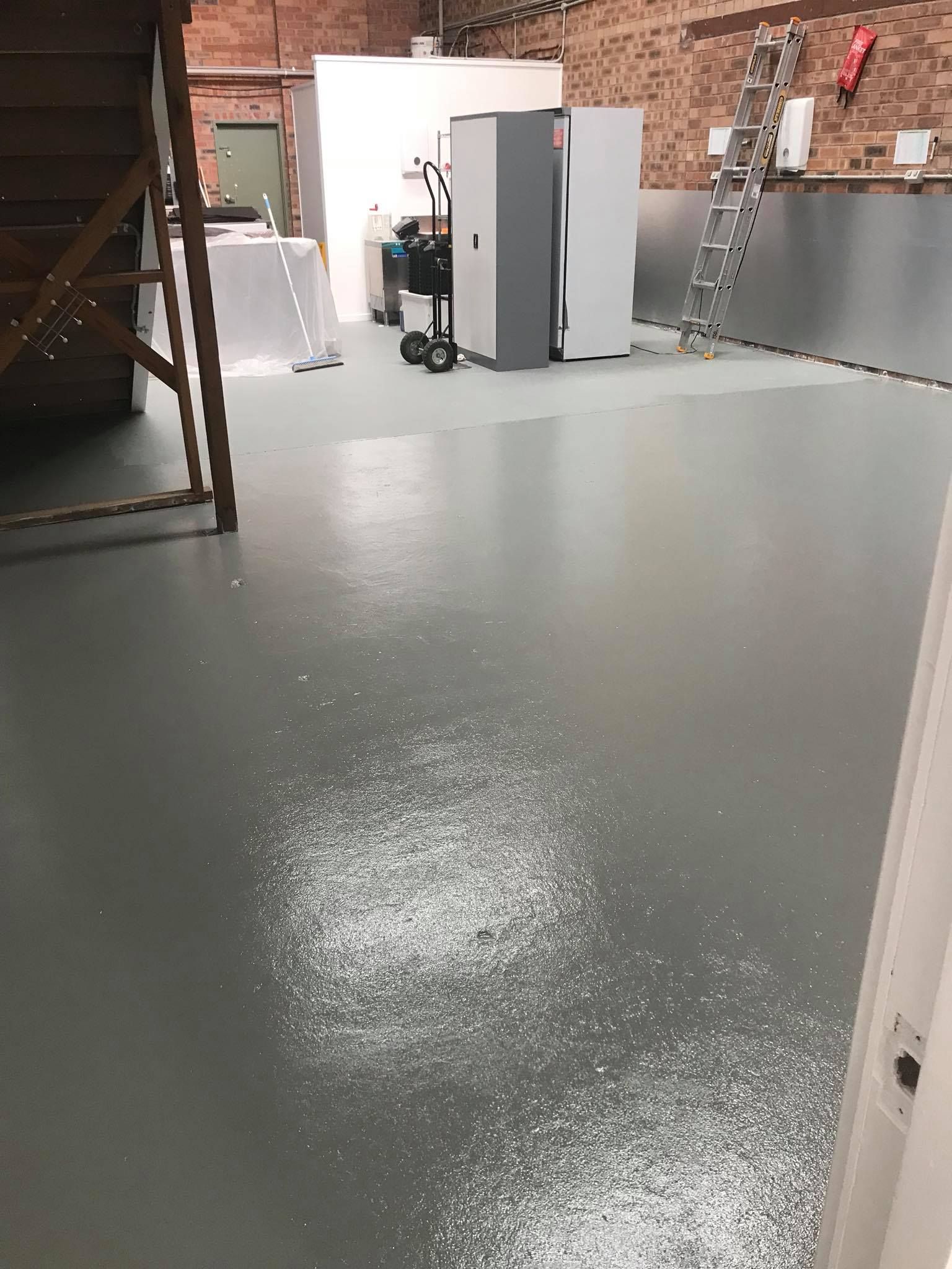 Gray painted floor with scattered white debris; a warehouse interior with appliances and a ladder.