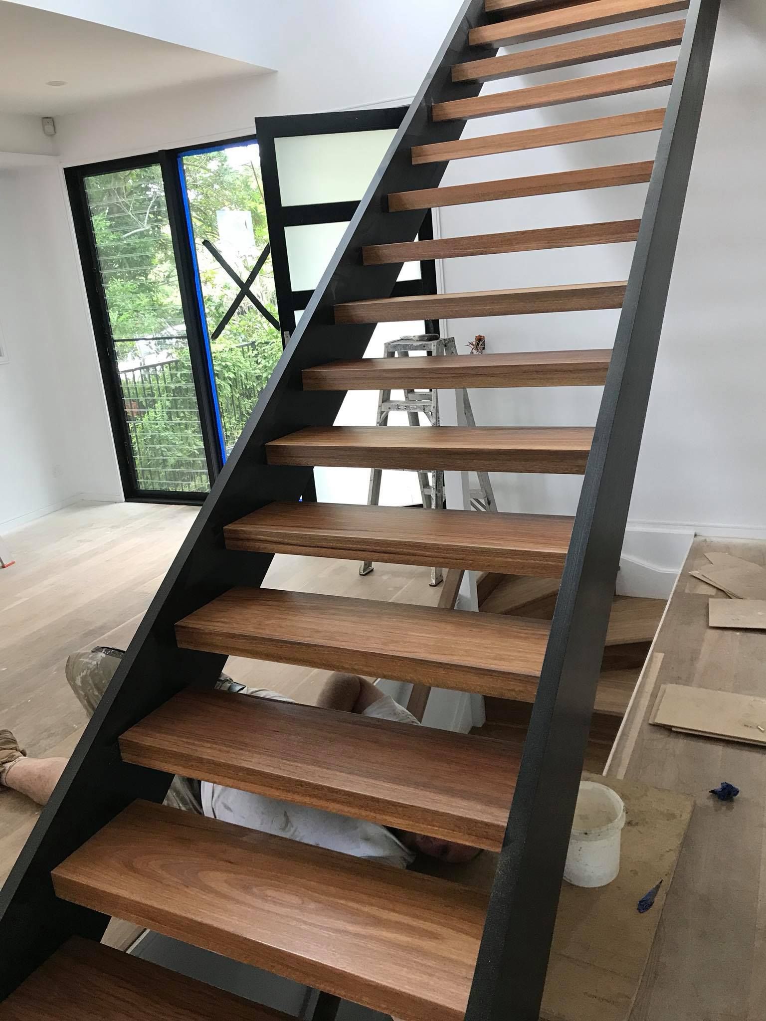 Wooden staircase with dark metal frame, visible construction materials in the background.
