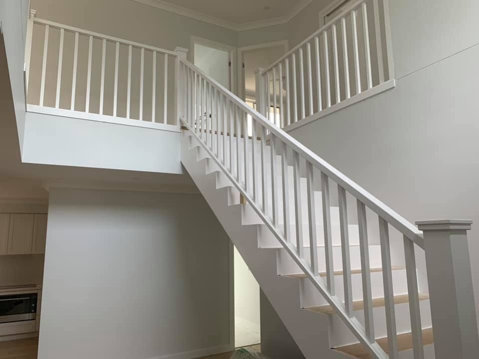 White staircase with railing, leading to a second floor. The walls are light grey.