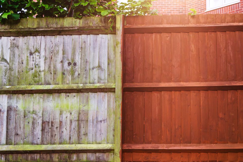 Wooden fence, half weathered and green, half stained brown.