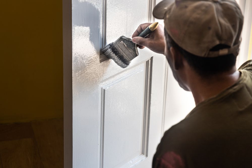 Person painting a white door with a paintbrush, in a well-lit room.
