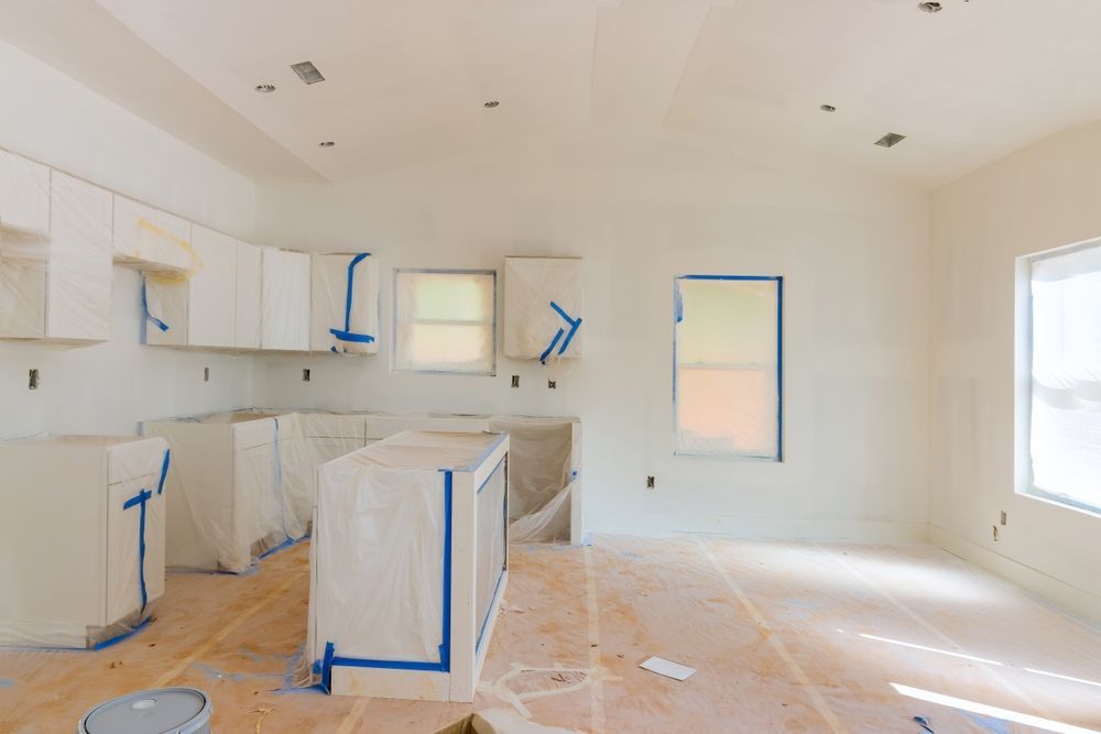 Kitchen under renovation with white cabinets, blue tape, and covered surfaces.