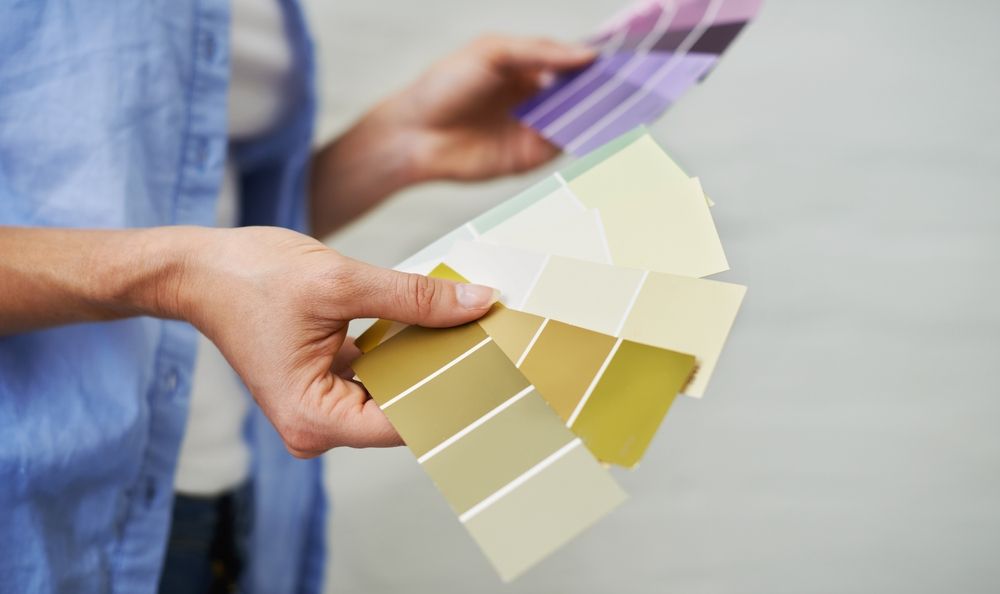 Person holding paint swatches, comparing shades of green, yellow, and purple.