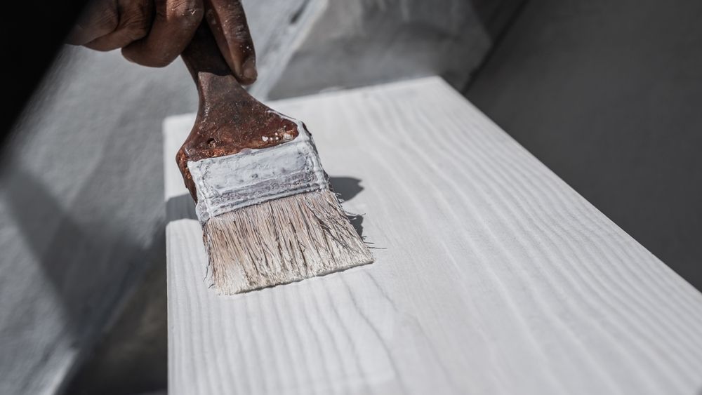 Hand painting a wooden surface with white paint using a brush.