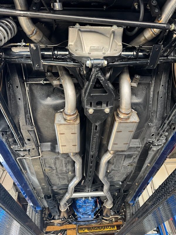 Underside of a vehicle on a lift, showing the exhaust system, rear axle, and suspension components against a black chassis.