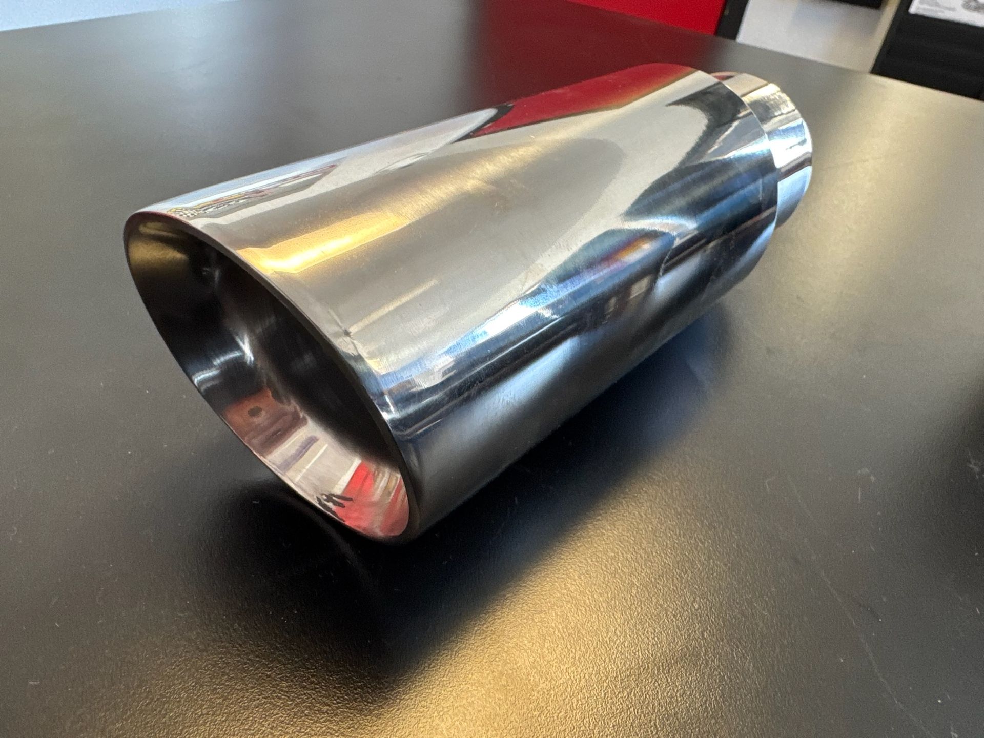 A polished, chrome-finished exhaust tip sits on a dark tabletop.