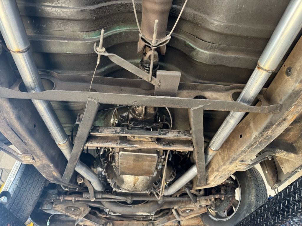 An underside view of a vehicle showing a custom fabricated steel frame, exhaust pipes, and transmission assembly.