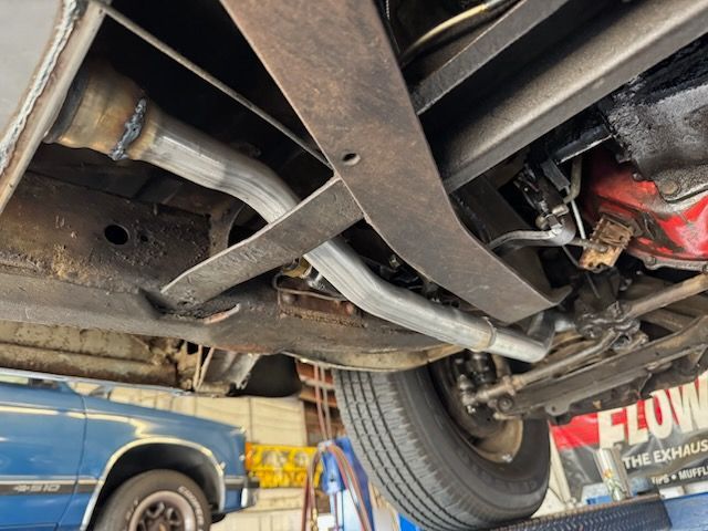 Low-angle view of a vehicle undercarriage showing new silver exhaust pipes installed beneath a red engine component.