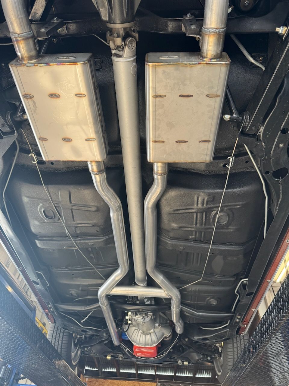 The underside of a vehicle showing a clean, recently installed dual exhaust system with stainless steel mufflers.