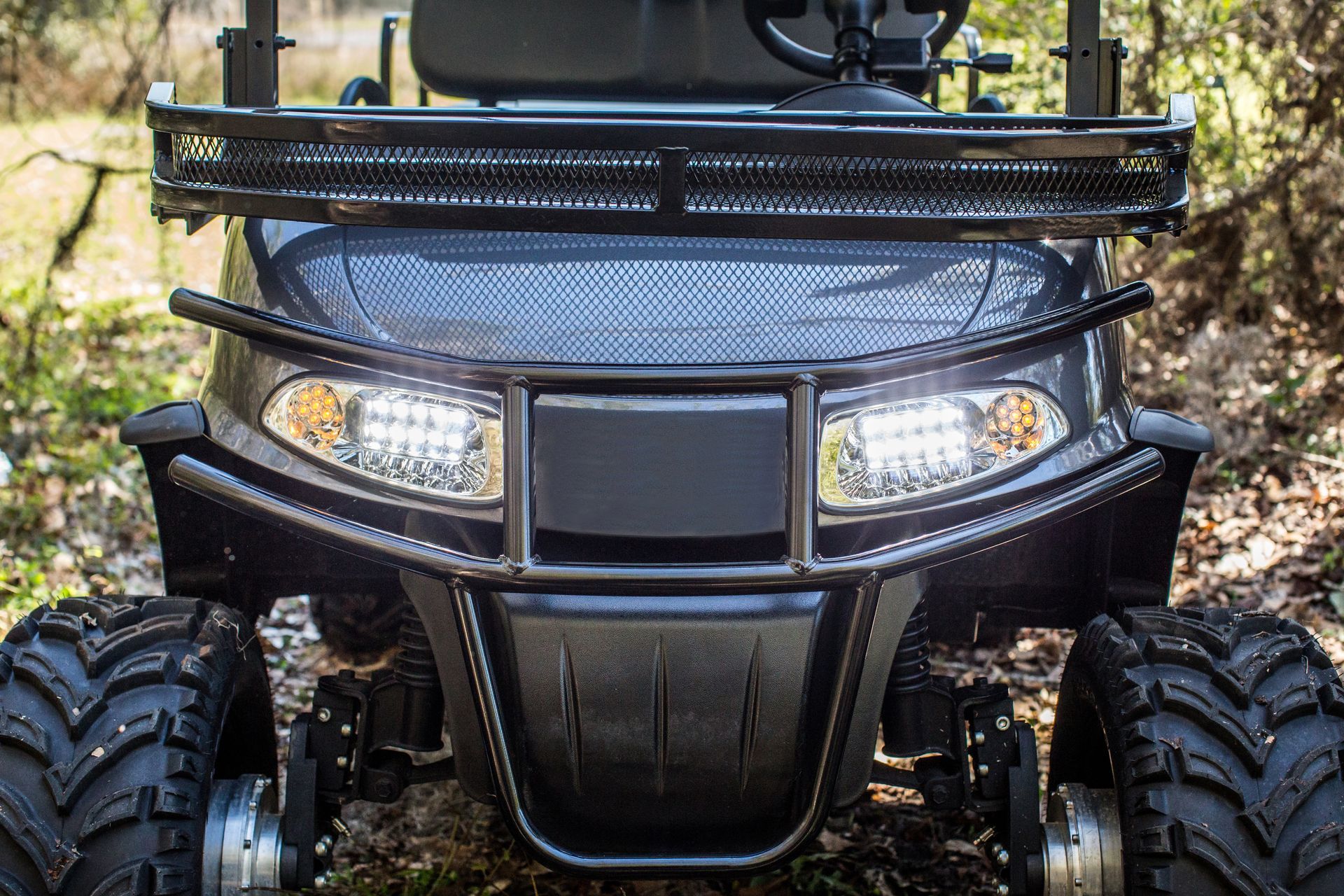 Front view of a black off-road ATV with bright headlights and large rugged tires outdoors