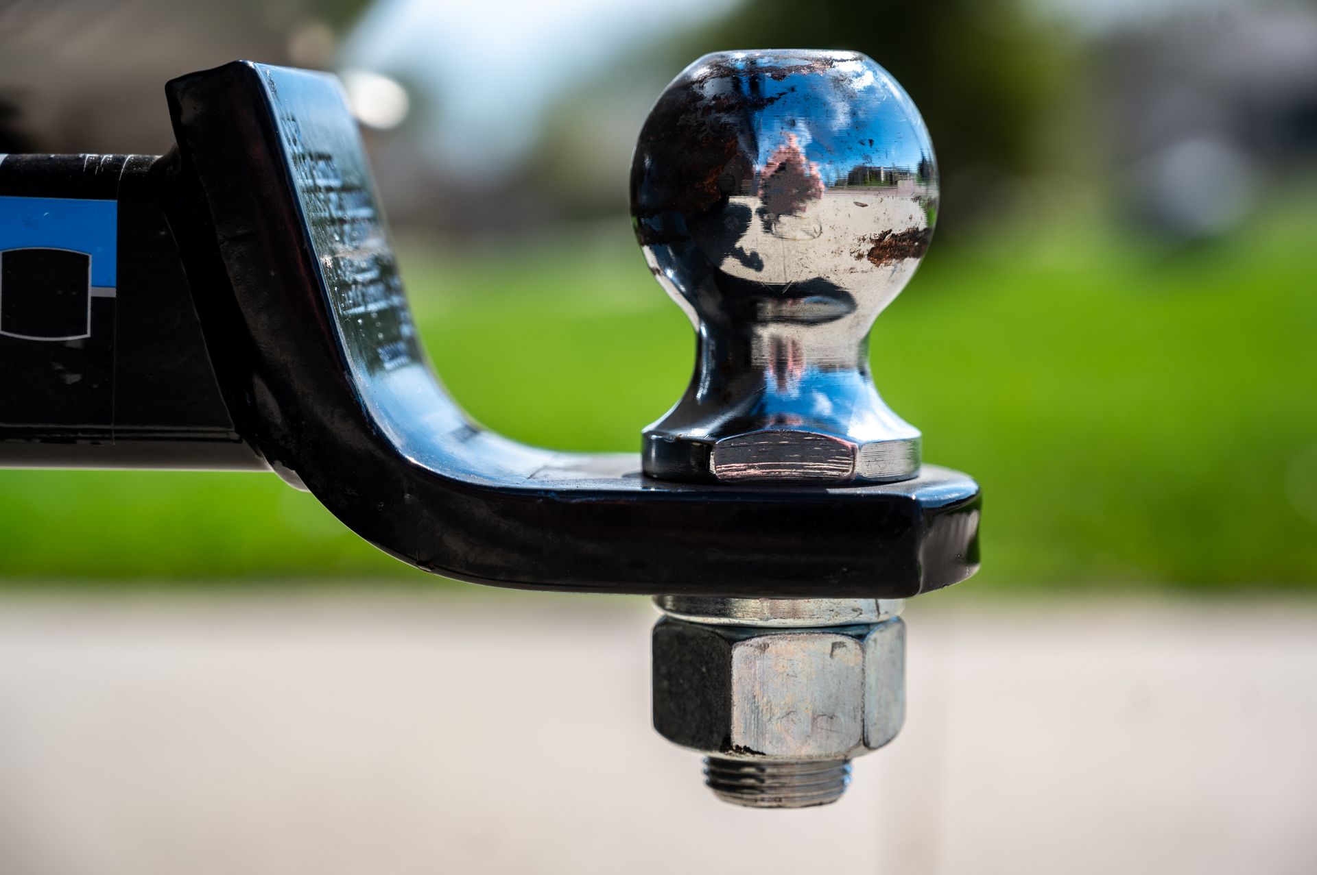 Close-up of a shiny trailer hitch ball on a black tow bar, with a blurred outdoor background