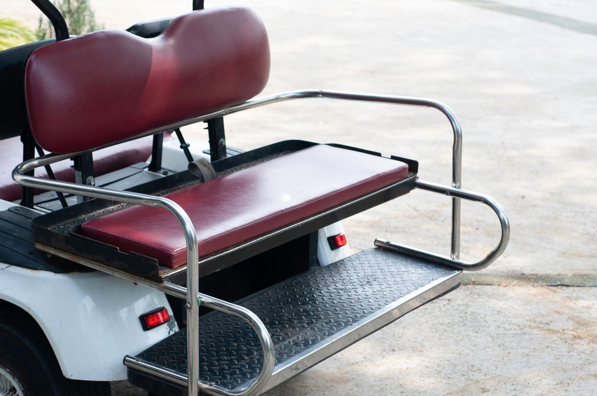 Maroon bench seat with chrome railings on a mobility cart platform outdoors