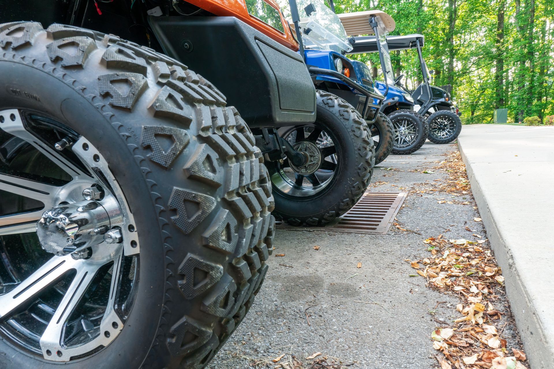 Row of parked all-terrain vehicles with large tires on a paved path beside trees
