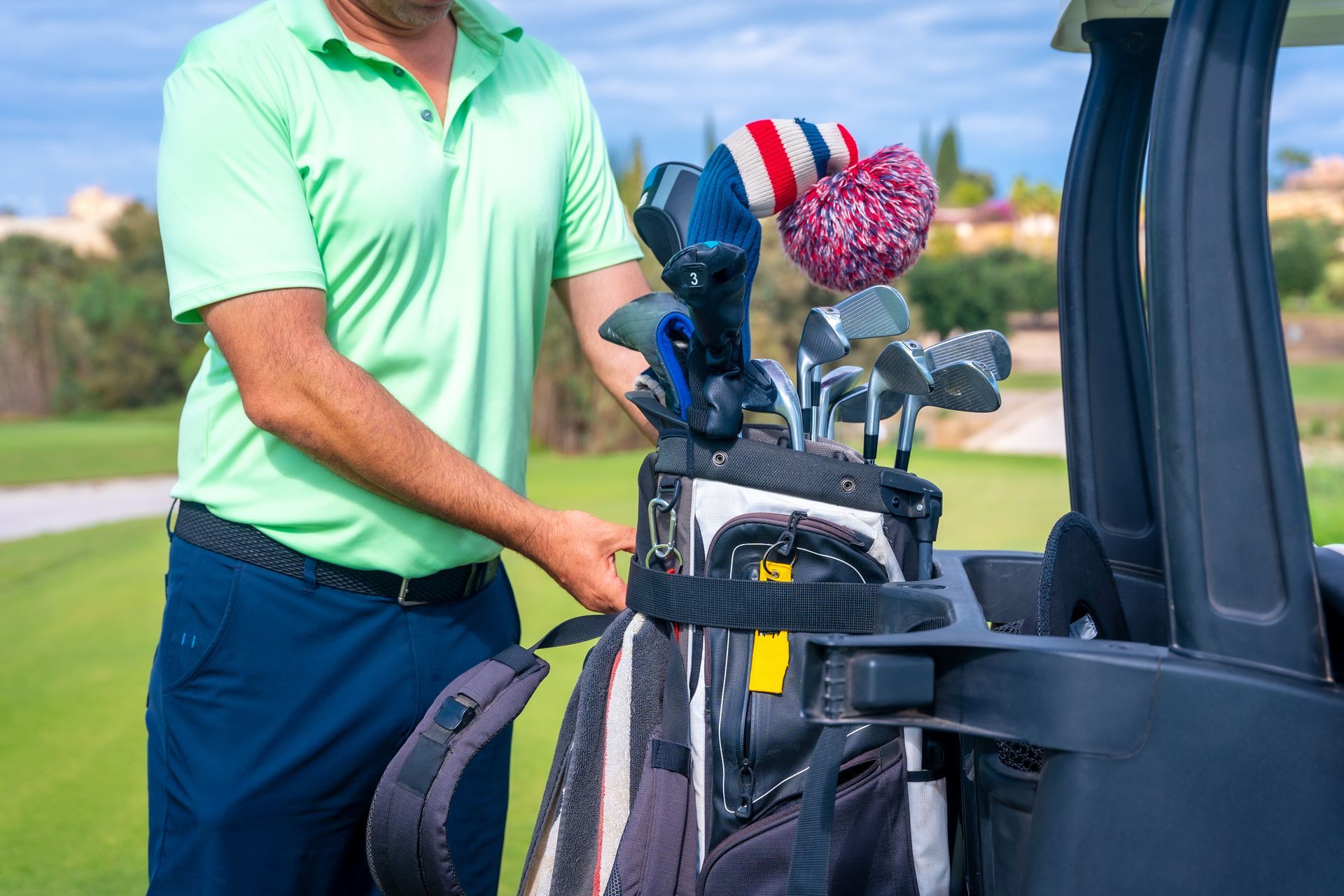 Golfer in a green shirt loading clubs into a golf cart on a sunny course