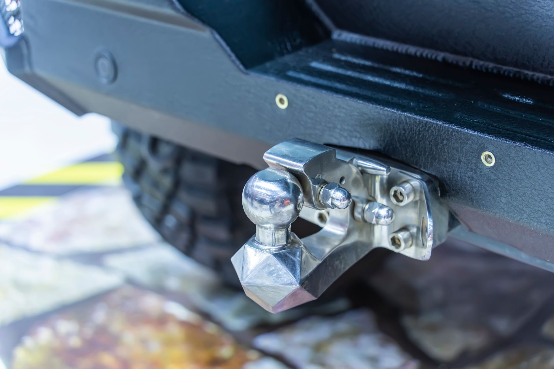 Close-up of a chrome trailer hitch ball mounted on a black vehicle bumper.