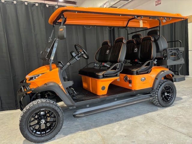 Orange six-seat electric utility cart with black trim and off-road tires indoors