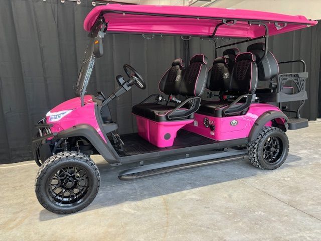 Pink four-seat golf cart with black roof parked outdoors against a gray wall